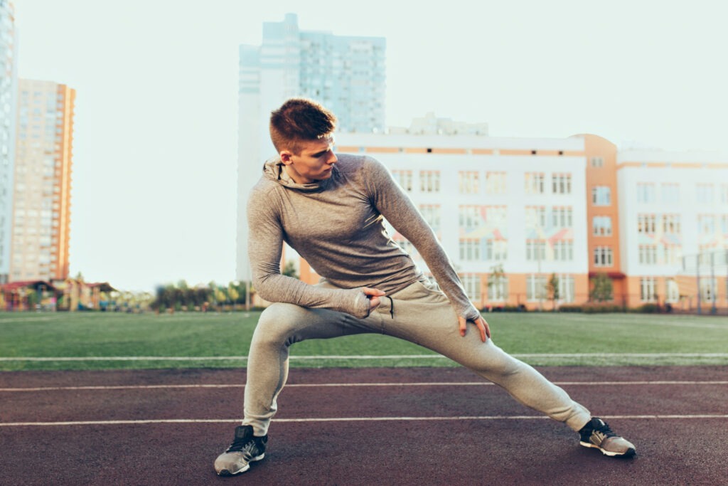 jeune-homme-sportif-entrainement-matin-stade-il-porte-costume-sport-gris-il-fait-etirements-5754997